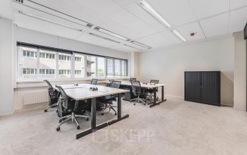 Lichte kantoorruimte met meerdere bureaus en stoelen, grote ramen en een uitzicht op een naastgelegen gebouw, ideaal voor kantoorruimte huren in Utrecht Centraal Station.