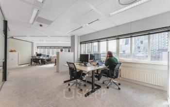 Kantoorruimte op Leidseveer 2-10 bij Utrecht Centraal Station met bureaus, stoelen en computers, waar mensen aan het werk zijn.