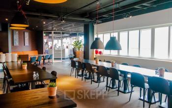 Kantoorruimte huren aan Leidseveer 2-10, Utrecht Centraal Station, met meerdere lange tafels en stoelen, geschikt voor vergaderingen of informele bijeenkomsten.