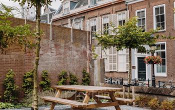 Buitenzijde van kantoorpand op Kromme Nieuwegracht 3, Utrecht Centrum met stenen zitplaatsen en tafels in een groene tuinomgeving.