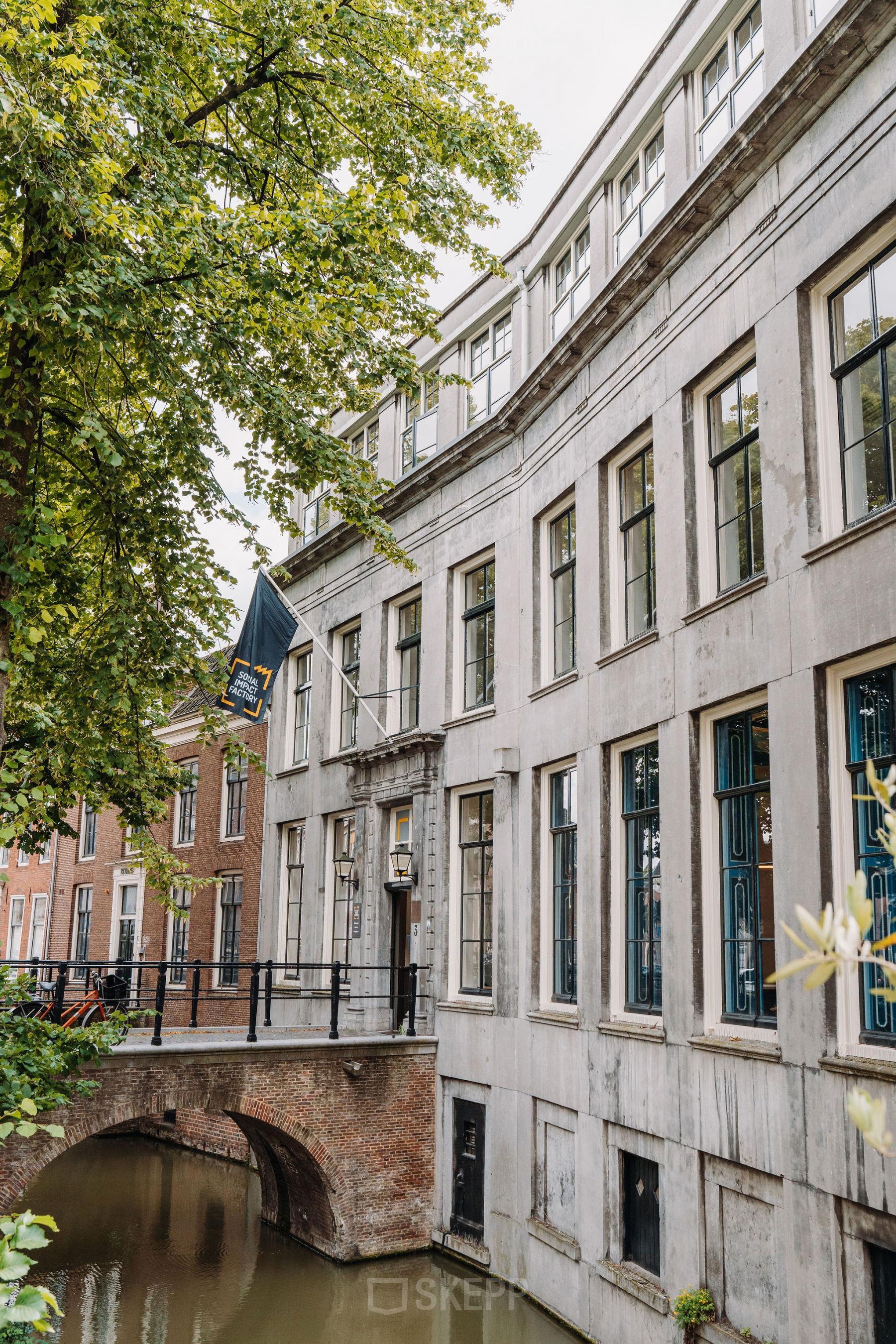 Utrecht Centrum kantoorpand aan de Kromme Nieuwegracht 3, gelegen aan een kanaal, met meerdere verdiepingen en vlag.