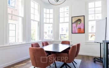 Moderne kantoorruimte huren bij Oudegracht 161, Utrecht Centrum: heldere vergaderruimte met houten vloer, comfortabele stoelen rond een tafel, met kunst aan de muur en veel natuurlijk licht binnen.
