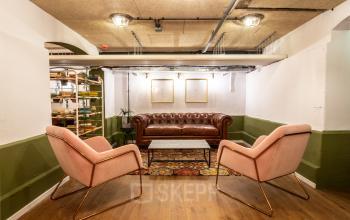 Gezellige lounge in kantoorpand Nicolaas Beetsstraat 216, Utrecht Centrum. Met retro leren bank, twee roze fauteuils, houten vloer en decoratieve tapijten.