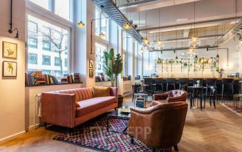 Kantoorpand op Nicolaas Beetsstraat 216 in Utrecht Centrum met sfeervolle inrichting, leren stoelen, een roze bank en hoge tafels. Planten en boekenrekken langs de muren.