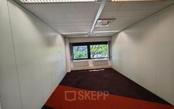 Leeg, goed verlichte kantoorruimte huren in kantoorpand op Bernadottelaan 13, Utrecht Kanaleneiland, met kleurrijke vloerbedekking en een groot raam voor natuurlijk licht.