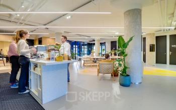 Moderne kantoorruimte in Utrecht Kanaleneiland, gelegen aan Europalaan 500, met open werkplekken, grote pilaren en ontmoetingstafel. Mensen in gesprek bij de pantry bijdragen aan een dynamische atmosfeer.