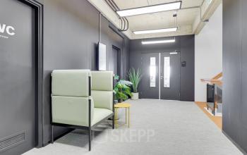 Neutrale gang bij kantoorpand op Europalaan 101, Utrecht Kanaleneiland, met zitgedeelte en planten. Ideaal voor wie kantoorruimte huren overweegt in deze bruisende omgeving. Glazen deuren geven toegang tot verder gelegen ruimtes.