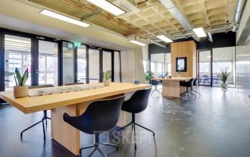 Ruim kantoorpand op Europalaan 101 in Utrecht Kanaleneiland met moderne inrichting. Twee grote houten tafels en comfortabele stoelen geschikt voor co-working ruimtes. De ruimte biedt veel natuurlijk licht en planten voor een frisse uitstraling.