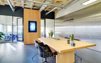 Vergaderruimte in kantoorpand Europalaan 101, Utrecht Kanaleneiland met moderne vergadertafel, stoelen en planten. Een groot scherm aan de muur biedt digitale presentatieopties. Ideale kantoorruimte huren voor zakelijke bijeenkomsten.