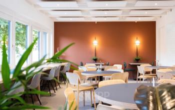 Moderne en uitnodigende bedrijfsruimte met ronde tafels en stoelen in een warme, gezellige sfeer op Atoomweg 50, Utrecht. Ideaal voor evenementen of als gemeenschappelijke werkruimte. Huur geschikt voor diverse bedrijfsactiviteiten.