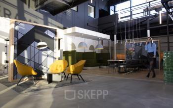 Moderne kantoorruimte op Atoomweg 63 in Utrecht Lage Weide met stijlvolle meubels, waaronder gele stoelen en een grote vergadertafel. Een vrouw voert een telefoongesprek. Ideaal voor kantoorruimte huren.