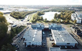 Luchtfoto van kantoorpand op Atoomweg 63, Utrecht Lage Weide, omgeven door groen en geparkeerde auto's. Perfecte locatie om kantoorruimte te huren met prachtig uitzicht over de omgeving.