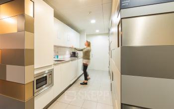 Kantoorruimte huren in Utrecht Leidsche Rijn met een moderne pantry, voorzien van keukenapparatuur waar een persoon een kopje koffie zet.