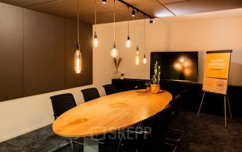 Vergaderruimte met een lange houten tafel, zwarte stoelen en sfeerverlichting, in een kantoorpand op Middenburcht 136, Utrecht Leidsche Rijn.