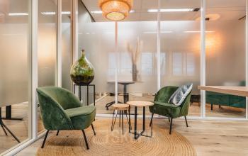 Stijlvolle lounge met groene stoelen, houten tafeltjes en moderne glazen scheidingswanden in kantoorpand Goeman Borgesiuslaan 77, Utrecht Noord. Ideaal voor kantoorruimte huren.