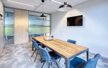 Vergaderruimte in kantoorpand op Mercatorlaan 1198-2000, Utrecht Papendorp. Kantoorruimte huren met houten vergadertafel, blauwe stoelen, televisie aan de muur en glazen scheidingswanden.