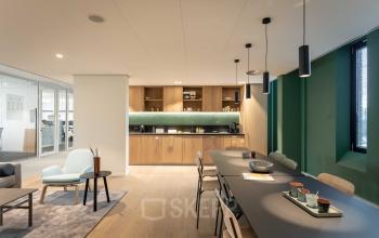 Een moderne en gemeubileerde kantoorruimte met een lange tafel, stoelen, een comfortabele zithoek en een pantry, ideaal om te huren in het kantoorpand aan Van Deventerlaan 31-51, Utrecht Papendorp.