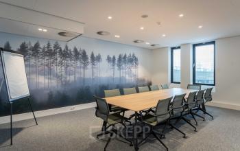 Vergaderruimte in kantoorpand op Van Deventerlaan 31-51, Utrecht Papendorp, met lange houten tafel en groene stoelen. Huur kantoorruimte met uitzicht op muurkunst van een boslandschap.