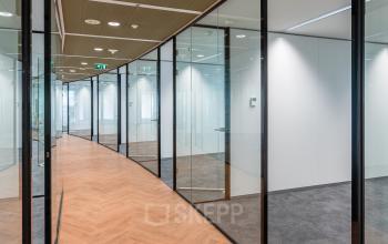 Modern ingerichte gang in kantoorpand op Newtonlaan 201, Utrecht Oost, met houten vloer en glazen wanden.