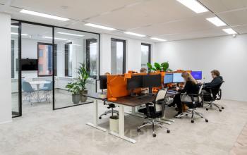 Modern kantoor met grote ramen en glazen wand, voorzien van bureaus met schermen waar personen aan het werk zijn in Utrecht Rijnsweerd.