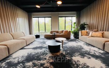 Gezellige zithoek in een kantoorpand aan de Varrolaan 100-126, Utrecht Rijnsweerd, met banken, ronde tafels en grote ramen die uitzicht bieden op groen. Ideaal voor werk of ontspanning.