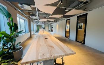 Stijlvolle kantoorruimte te huur op Varrolaan 100-126, Utrecht Rijnsweerd, met lange houten tafel, moderne plafonddecoratie en groene planten.