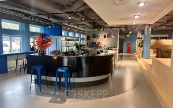 Lichte kantoorruimte huren op Daltonlaan 200 in Utrecht Rijnsweerd met een moderne bar, blauwe krukken en kleurrijke decoraties voor een informele werk- of pauzeomgeving.