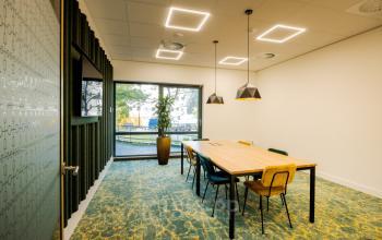 Moderne vergaderruimte in een kantoorpand aan de Euclideslaan 51, Utrecht Rijnsweerd, met lange houten tafel, kleurrijke stoelen en grote ramen. Ideale plek om kantoorruimte te huren voor inspirerende bijeenkomsten.