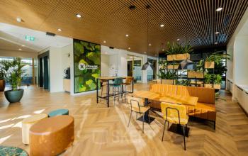 Moderne kantoorruimte huren in Utrecht Rijnsweerd met open indeling, natuurlijke houten plafondpanelen en groene accenten, inclusief uitnodigende zitplaatsen en veel lichtinval.