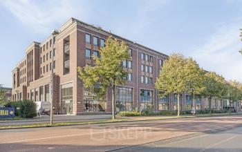 Bakstenen kantoorpand op Niasstraat 1 in Utrecht West, met moderne architectuur en grote ramen. Kantoorruimte huren in een centrale, dynamische omgeving. Groene bomen langs de straat zorgen voor een aangename omgeving.