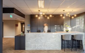 Moderne receptie in kantoorpand met stijlvolle balie en zitplekken, gelegen op Niasstraat 1 1 in Utrecht West. Een medewerker is bezig met een zakelijke activiteit.