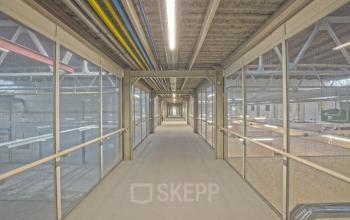 Industrieel ogende gang in het kantoorpand op Eendrachtlaan 100-260, Utrecht Zuid, met glazen wanden en zicht op naastgelegen ruimtes. Kantoorruimte huren in een uniek pand.