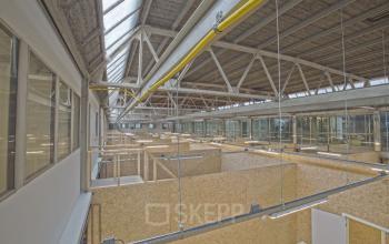 Een ruime en lichte kantoorruimte met zichtbare constructie en OSB-materiaal, geschikt voor het huren van diverse werkplekken in een industrieel kantoorpand in Utrecht Zuid.