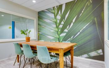 Gezellige vergaderruimte met houten tafel en blauwe stoelen, in kantoorpand Kanaalweg 22, Utrecht Zuid, ideaal voor kantoorruimte huren. Grote groene wanddecoratie geeft levendige uitstraling.