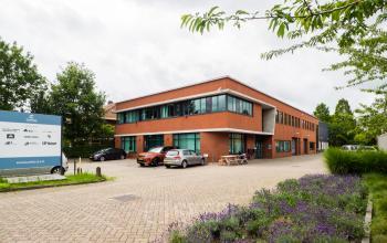 Kantoorpand Kanaalweg 22 in Utrecht Zuid, met een bakstenen gevel en grote ramen, omringd door parkeerplaatsen en groen. Geschikt voor bedrijven die kantoorruimte willen huren met goede bereikbaarheid.