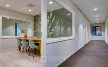 Kantoorpand aan de Kanaalweg 22 in Utrecht Zuid met gang en vergaderruimte uitgerust met houten tafel en stoelen. Glaswanden zorgen voor een open en lichte sfeer, ideaal voor een kantoorruimte huren.