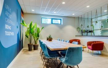 Kantoorruimte huren op Kanaalweg 22, Utrecht Zuid: modern ingerichte vergaderruimte met houten tafel, blauwe stoelen en planten aan de muur; ideaal voor zakelijke bijeenkomsten in een inspirerende omgeving.