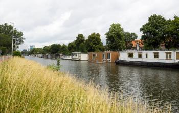 Uitzicht op het water bij Kanaalweg 22, Utrecht Zuid, met woonboten langs het kanaal, omgeven door groene bomen.