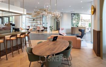 Moderne kantoorlounge met houten tafel en groene stoelen, bar met krukken en comfortabele zitplaatsen in kantoorpand op Europalaan 40, Utrecht Zuid. Gezellige plek om te werken of vergaderen.