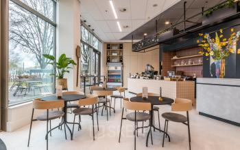 Moderne kantine in kantoorpand aan de Vliegend Hertlaan 15, Utrecht Zuid. De ruimte is ingericht met tafels en stoelen, geschikt voor bijeenkomsten of pauzes. Grote ramen bieden uitzicht naar buiten.