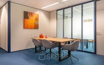Zakelijke vergaderruimte in kantoorpand Vendelier 61, Veenendaal, modern ingericht met houten tafel en zes stoelen, kleuraccenten in oranje en blauw. Perfecte locatie voor kantoorruimte huren.