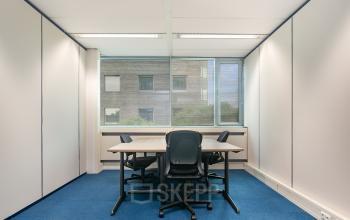 Kantoorruimte op Vendelier 61 in Veenendaal met blauwe vloerbedekking, een tafel en drie stoelen. Grote ramen bieden uitzicht naar buiten.