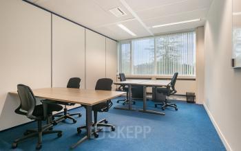 Zicht op een functionele kantoorruimte in Vendelier 61, Veenendaal met blauwe tapijt en grote ramen. Ideaal om te huren als werkplek met meerdere bureaus en stoelen.