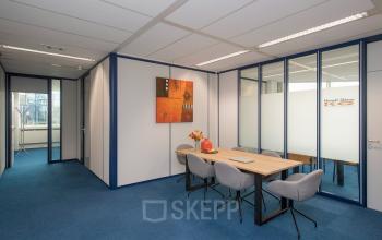 Kantoorruimte huren in Veenendaal: Vendelier 61 biedt een vergaderruimte met blauwe vloeren en glazen wanden. Een tafel met stoelen is ingericht voor vergaderingen of teamoverleggen.