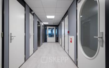 Ruime hal in kantoorpand Vendelier 59, Veenendaal, met lichte muren en deuren, ideaal voor kantoorruimte huren. Strakke afwerking met helder, natuurlijk licht door ramen aan het einde van de gang.