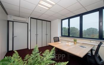 Moderne kantoorruimte in kantoorpand aan Vendelier 59 in Veenendaal met bureau en vergaderstoelen, grote ramen en groene planten.