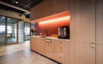 Een moderne pantry in een kantoorpand op Doornhoek 3745, Veghel, met strakke houten kasten en een koffiezetapparaat, ideaal voor pauzes tijdens het huren van een kantoorruimte.