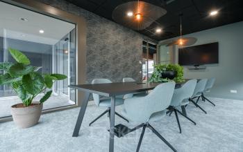 Moderne vergaderruimte met grijze stoelen en een groot scherm aan de muur in kantoorpand Doornhoek 3745, Veghel. Planten zorgen voor een frisse uitstraling. Ideaal om een kantoorruimte te huren.