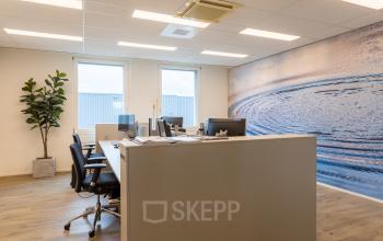 Kantoorruimte huren op Costerweg 5 in Veghel met moderne werkplekken, bureaus en stoelen, voorzien van natuurlijke verlichting en decoratief kunstwerk op de muur.