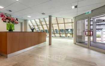 Ingang van een kantoorpand op De Run 1141-1157 in Veldhoven met grote ramen, ontvangstbalie en bloemenvaas. Ideaal voor bedrijven die kantoorruimte willen huren.